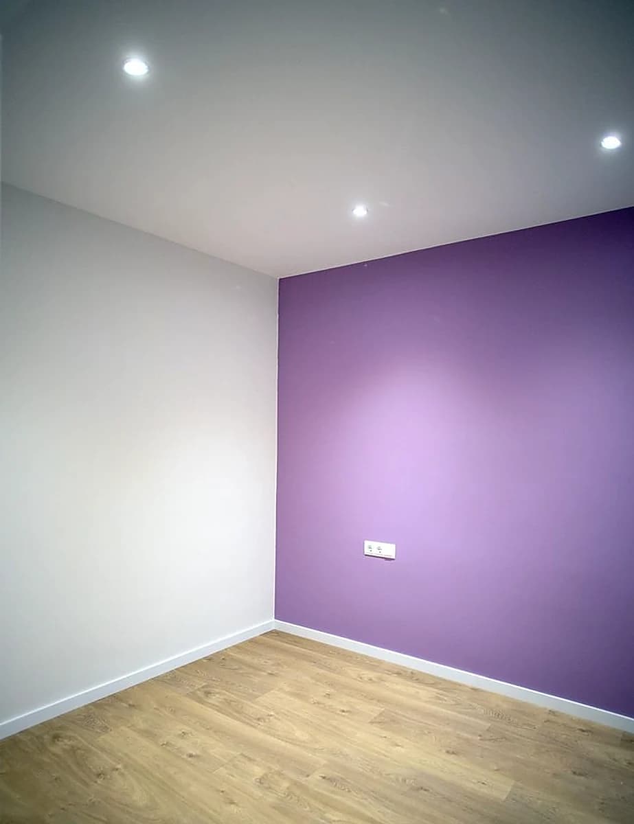 Stanza tinteggiata di bianco con una parete a contrasto viola e parquet chiaro